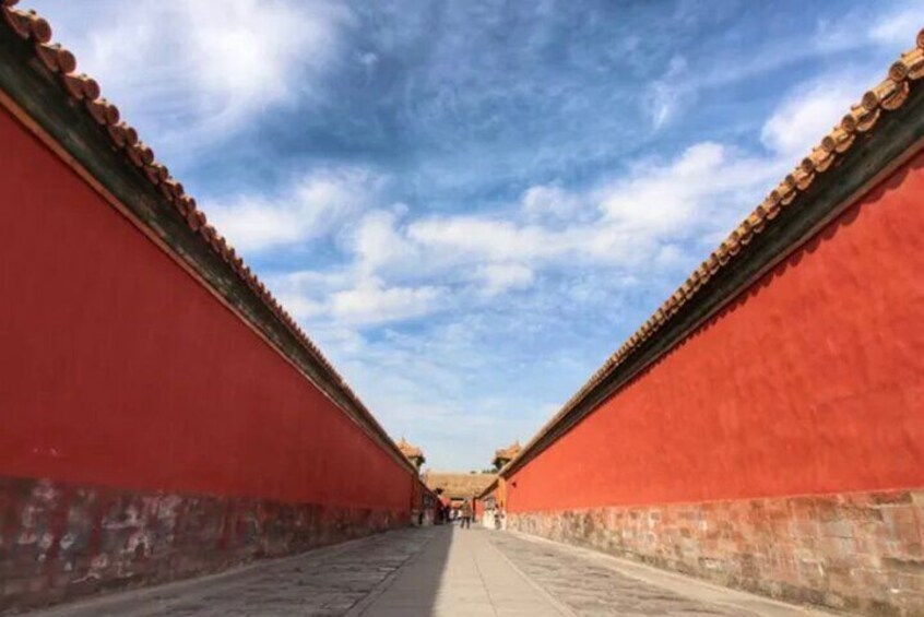 A corridor with red walls and a tiled roof, leading to a distant structure. 5