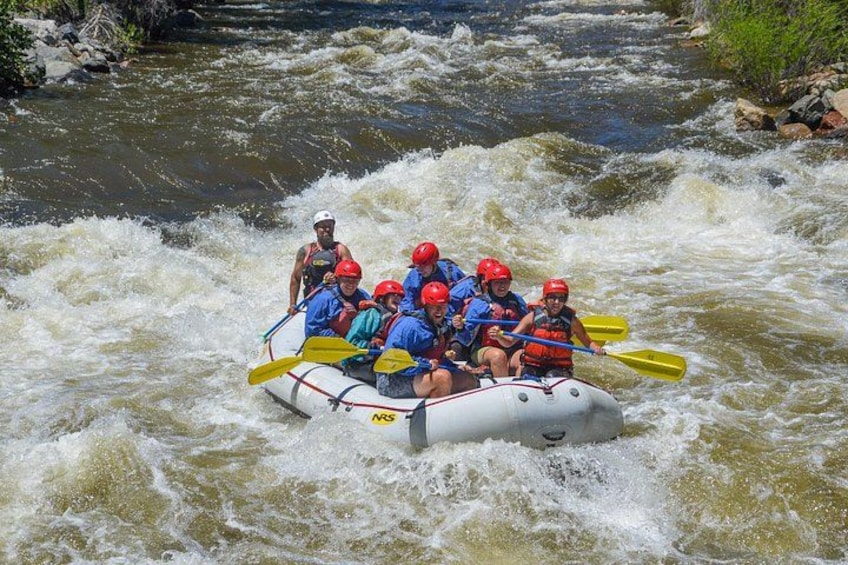 A group of people in a white inflatable raft navigating a river with rapids. 5