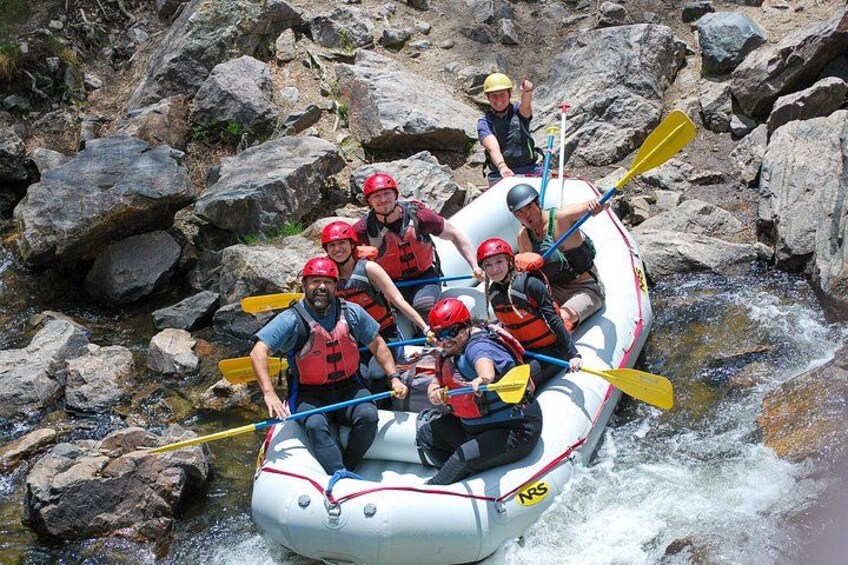 A group of people in a white inflatable raft navigating a river with rapids, surrounded by large rocks. 4