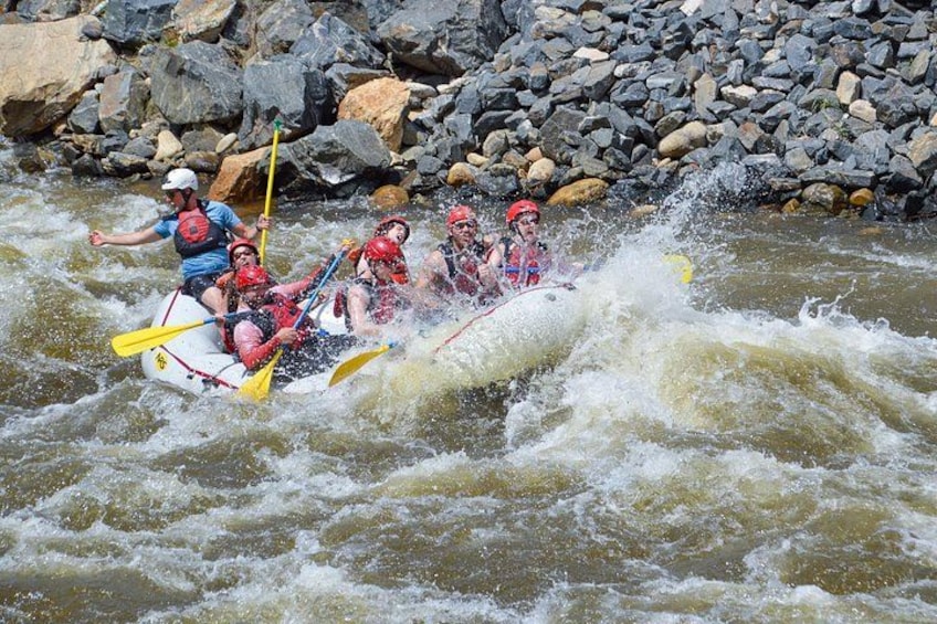 A group of people rafting on a river with turbulent water and a rocky riverbank. 1