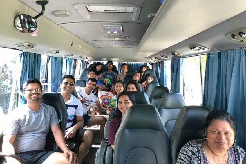 A group of people seated inside a bus with blue curtains and black seats. 4