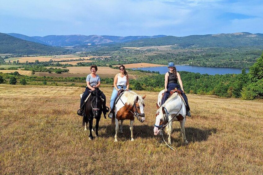Drei Personen reiten Pferde durch ein grasbewachsenes Feld mit einem See und Bergen im Hintergrund. 5
