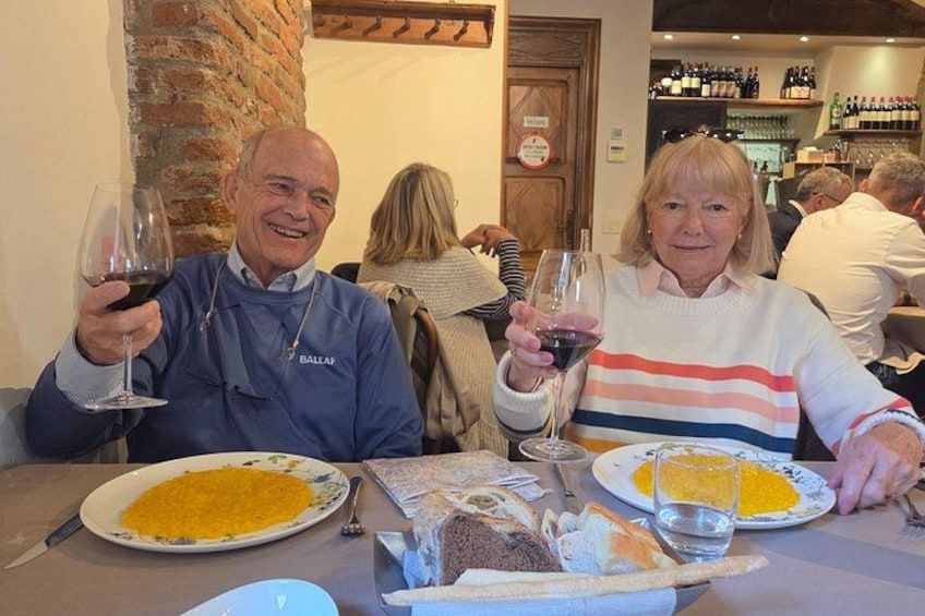 Two people sitting at a table with plates of food and wine glasses. 1