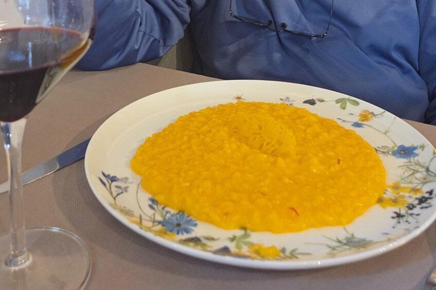 A plate of yellow rice on a floral plate, a wine glass with red wine, and a knife on a table. 4