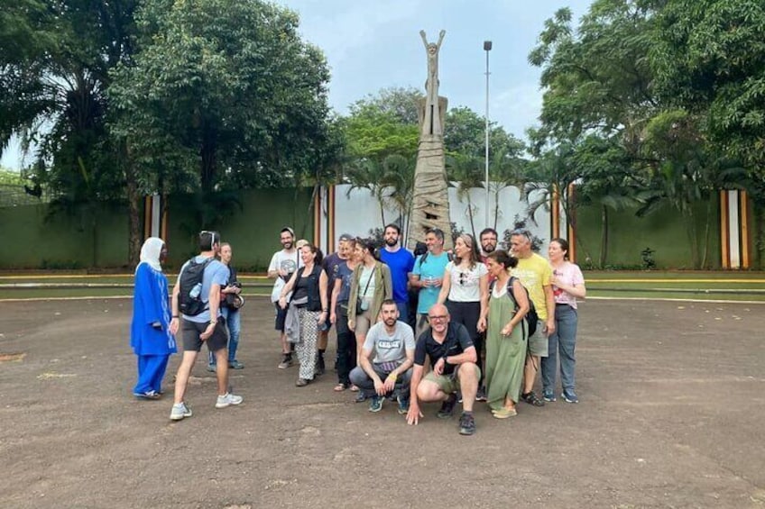 Un groupe de personnes posant pour une photo dans un cadre extérieur, avec des arbres et une sculpture en arrière-plan. 1