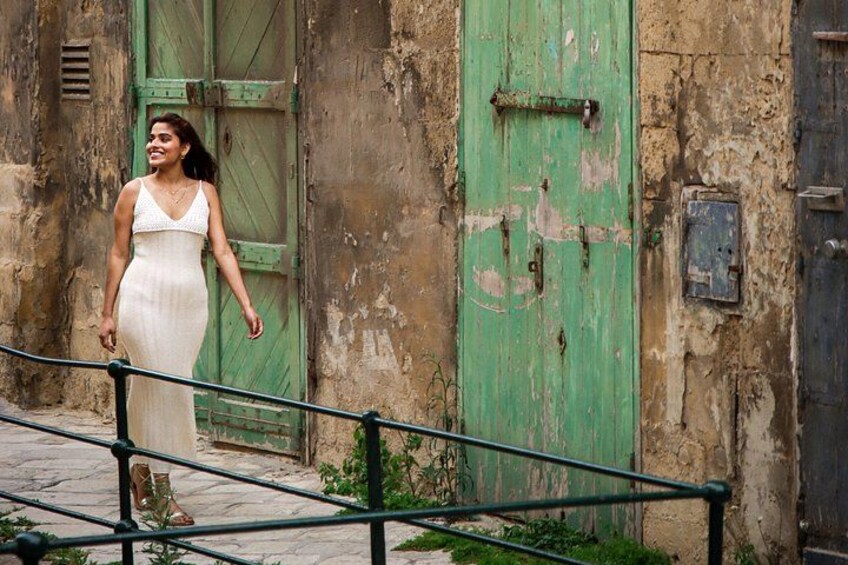 Una mujer con un vestido blanco camina cerca de una puerta verde y un muro desgastado. 4