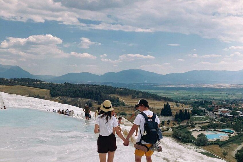 A group of people hiking near a geothermal area with a pool of water and distant mountains. 3