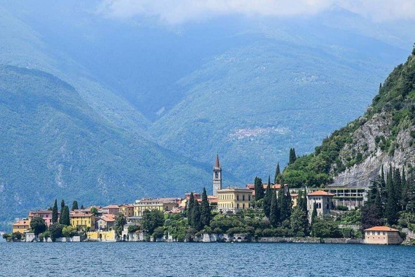 A lakeside town with buildings, a church, and mountains in the background. 3