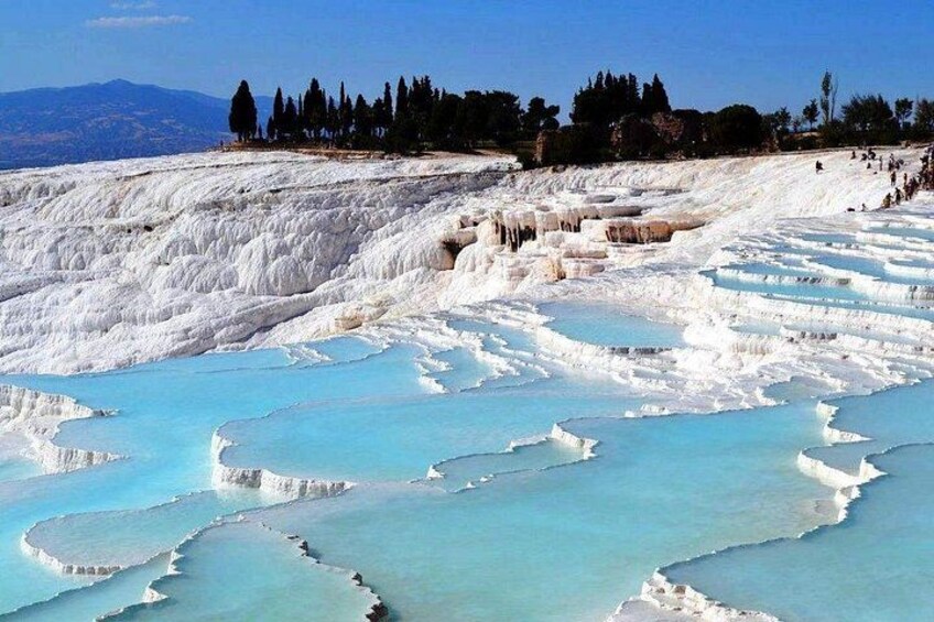 Terraced mineral pools, a clear sky, and distant trees. 4