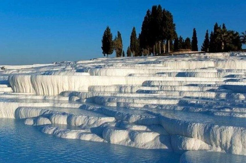 Terraced travertine formations, trees, and a clear blue sky. 3