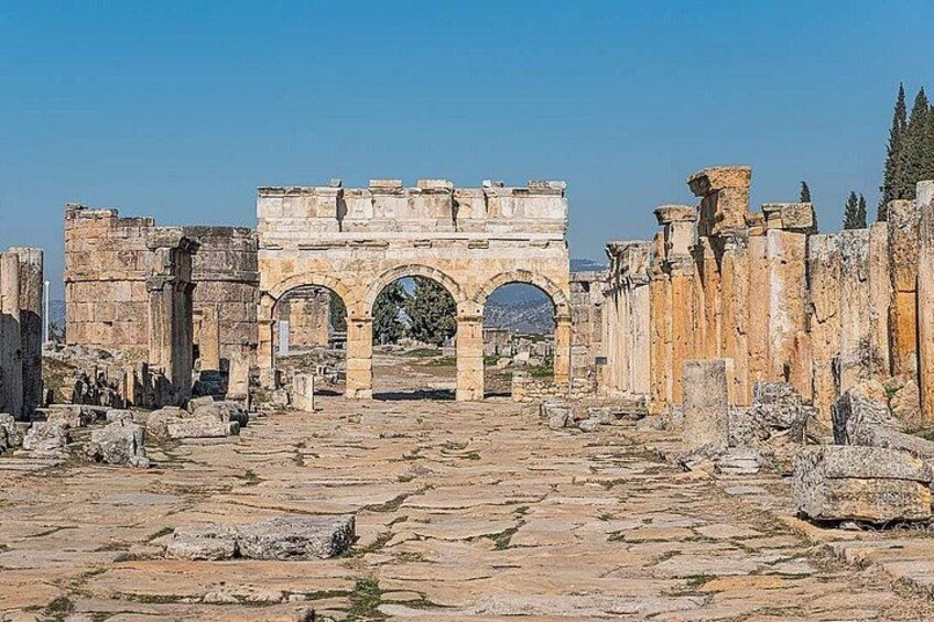 Ancient ruins with an arched gateway, stone columns, and scattered debris. 1