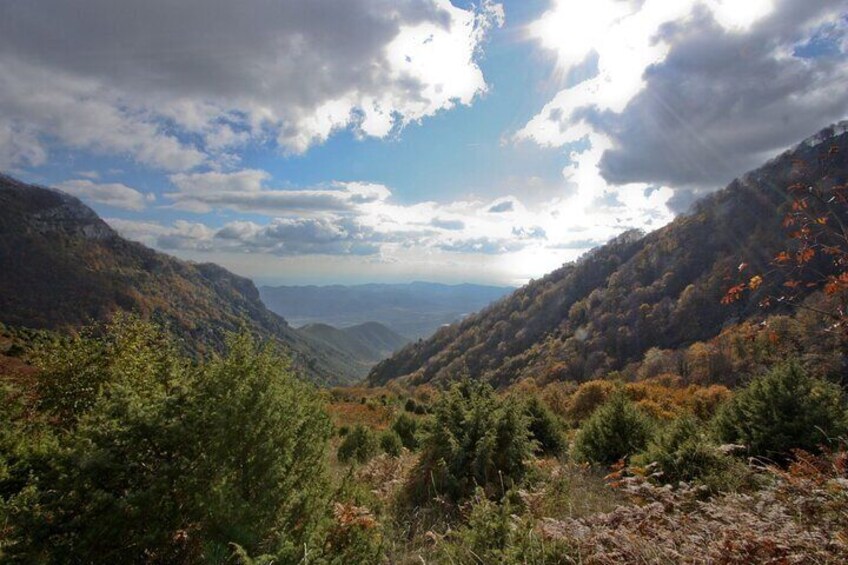 A mountainous landscape with autumn foliage, a valley, and distant hills under a partly cloudy sky. 3
