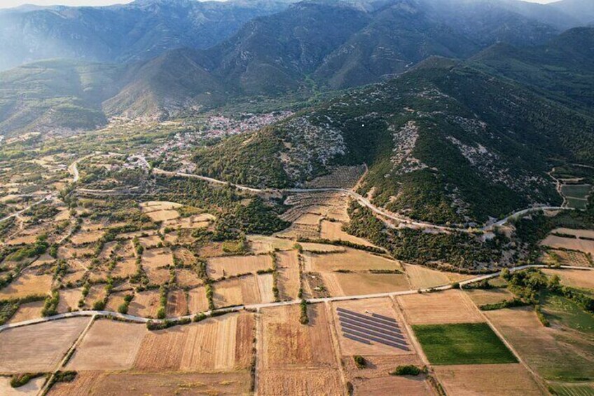 An aerial view of a valley with terraced fields, a winding road, and a small settlement. 2