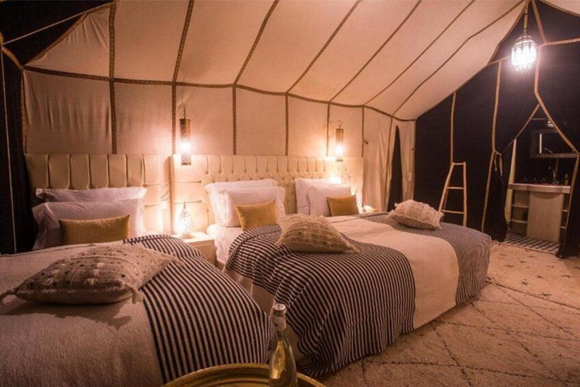 A tented accommodation with a large bed, pillows, and a bedside table. 5