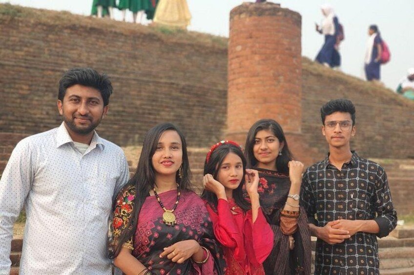 A group of people standing in front of a brick structure with a cylindrical tower. 1