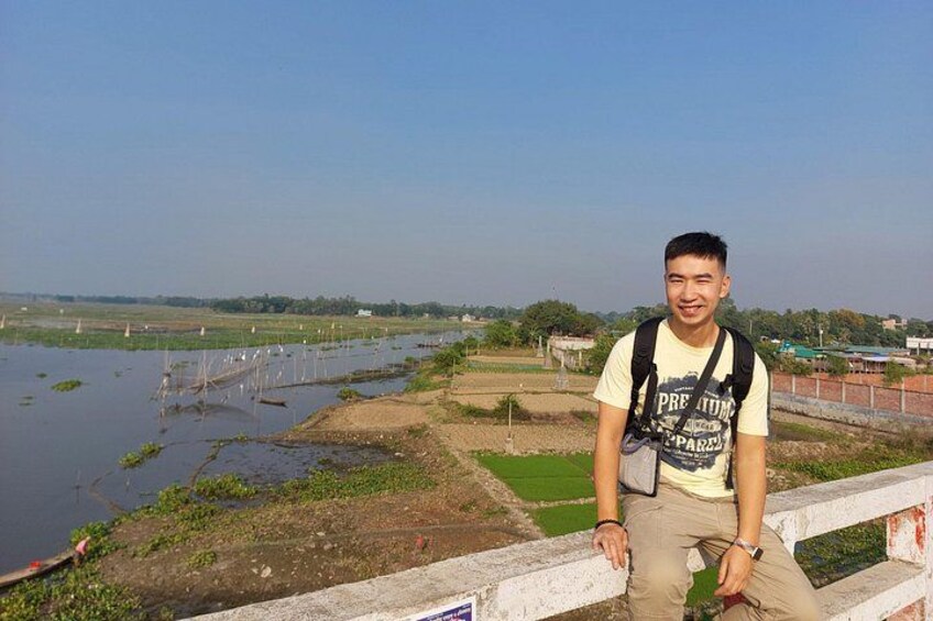 A person standing on a concrete barrier overlooking a water body with vegetation and distant structures. 3
