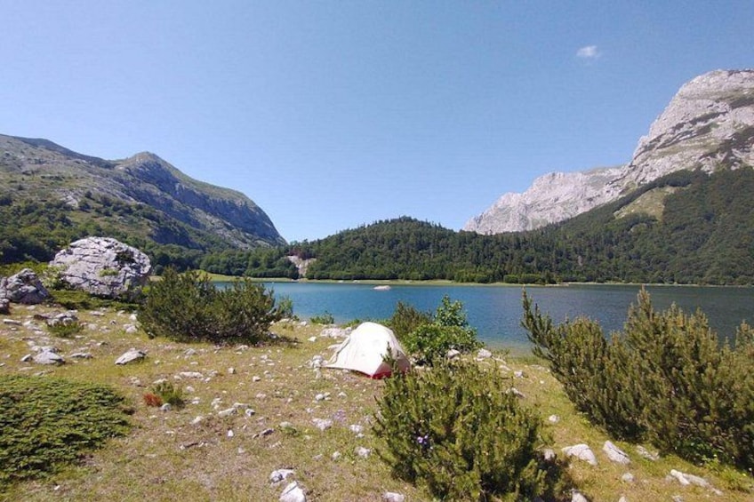 A tent on a grassy area near a lake surrounded by mountains. 4