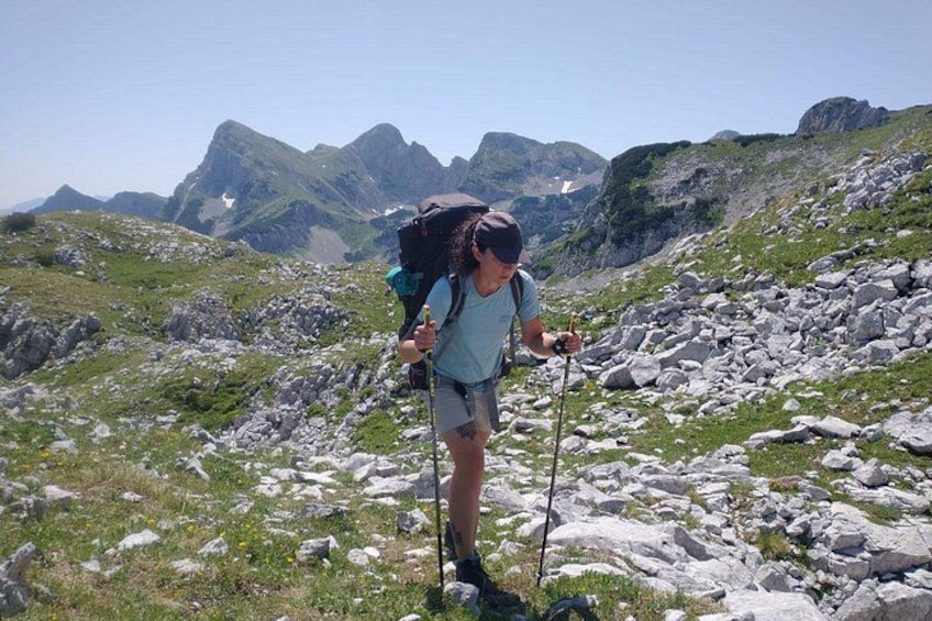 A hiker with a backpack and walking poles on a rocky mountain trail. 3