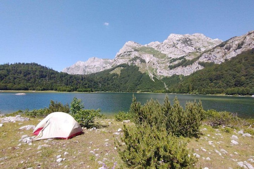 A tent on a grassy shore, a lake, and mountains in the background. 1