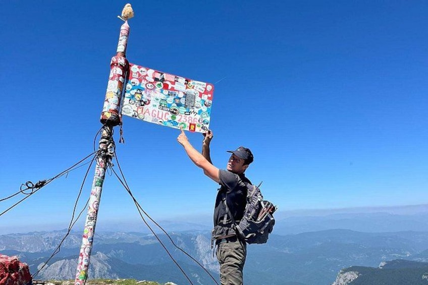 A person standing on a mountain peak, holding a sign with stickers. 2