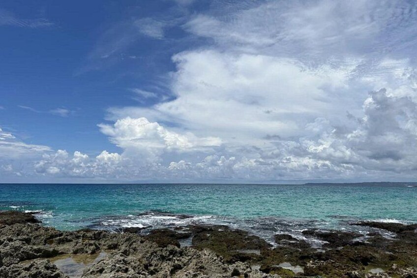 A rocky shoreline with clear turquoise water and a partly cloudy sky. 2