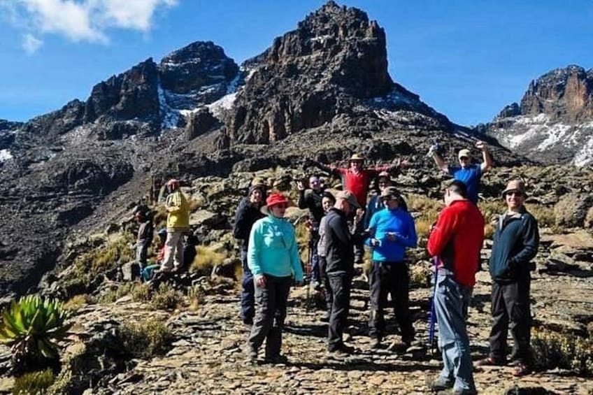 A group of people standing on a rocky mountain terrain with a prominent peak in the background. 1