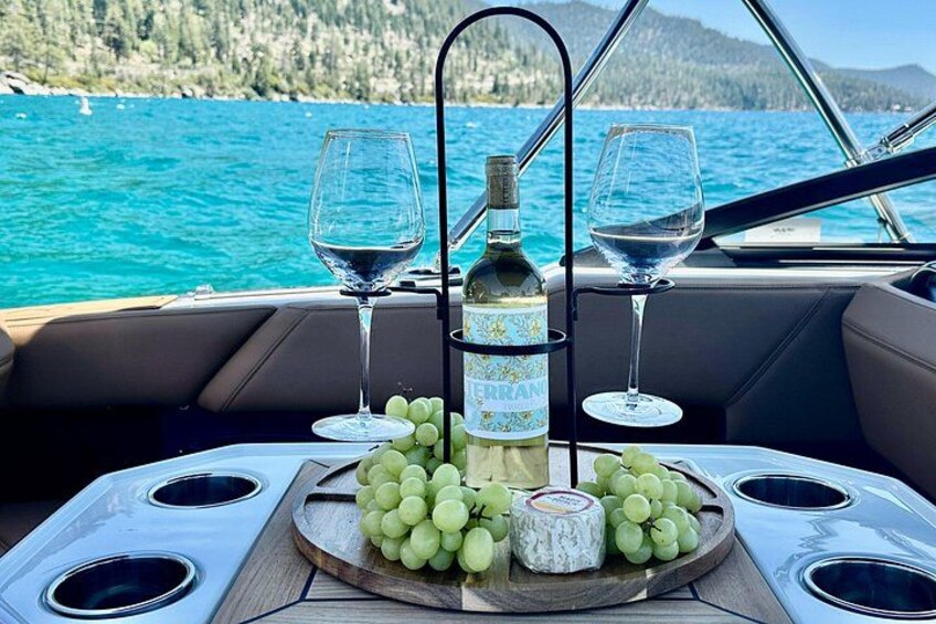 A boat interior with a table set for a meal, featuring a bottle of wine, glasses, and a plate of grapes. 2