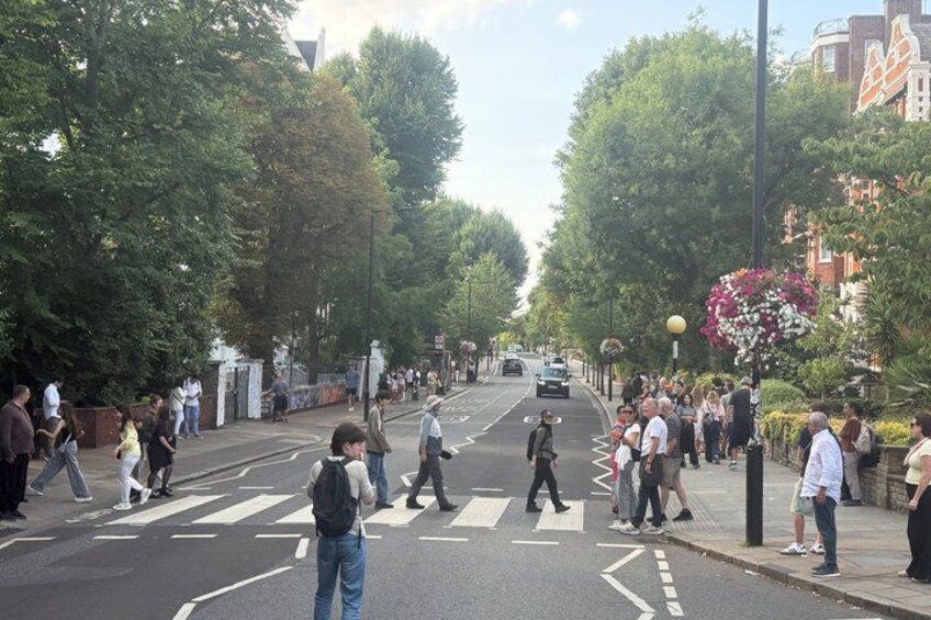 Une rue animée en milieu urbain, avec des piétons qui la traversent, des arbres bordant les trottoirs et des bâtiments en arrière-plan. 3