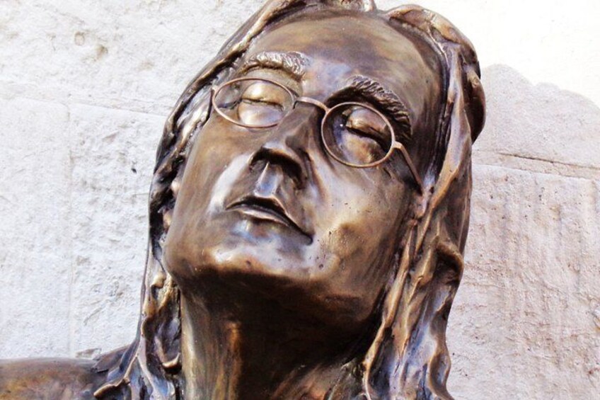 A bronze sculpture of a person with glasses, set against a stone wall. 1