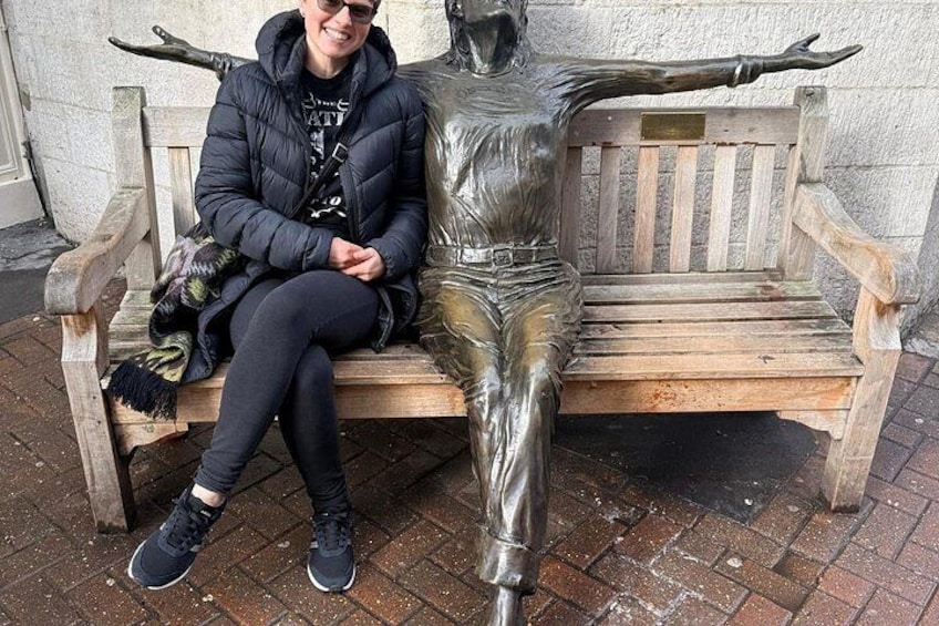 A person sitting on a bench with a statue of a figure with outstretched arms. 4