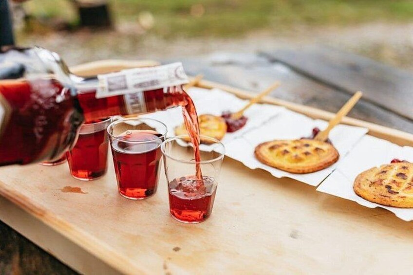 A wooden table with a pitcher pouring red liquid into glasses, and a cookie on a stick. 5