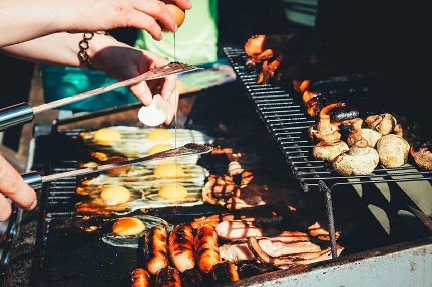 A person grilling various foods including sausages, eggs, and mushrooms on a barbecue. 2