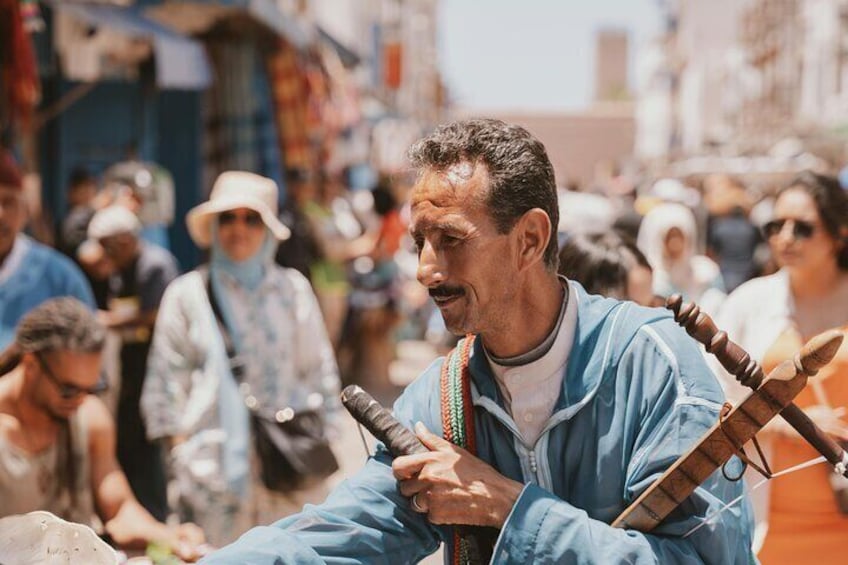 A man playing a traditional stringed instrument in a crowded outdoor market. 5