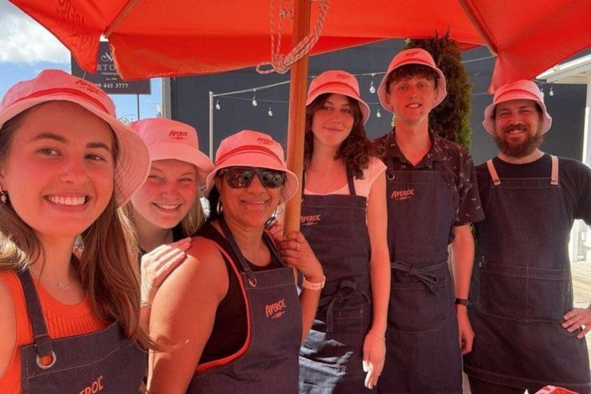 A group of people wearing matching aprons and hats, standing under a red umbrella. 5