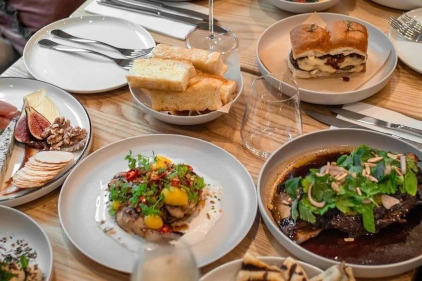 A variety of dishes on a wooden table, including a plate with sliced meat, a bowl of salad, and a dish with a dark sauce. 1