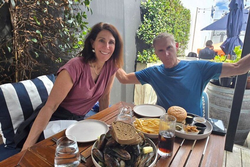 Two people sitting at an outdoor table with food and drinks. 3