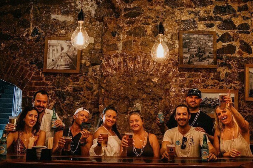 Un groupe de personnes se trouve dans un bar aux murs de pierre et aux ampoules suspendues. 3