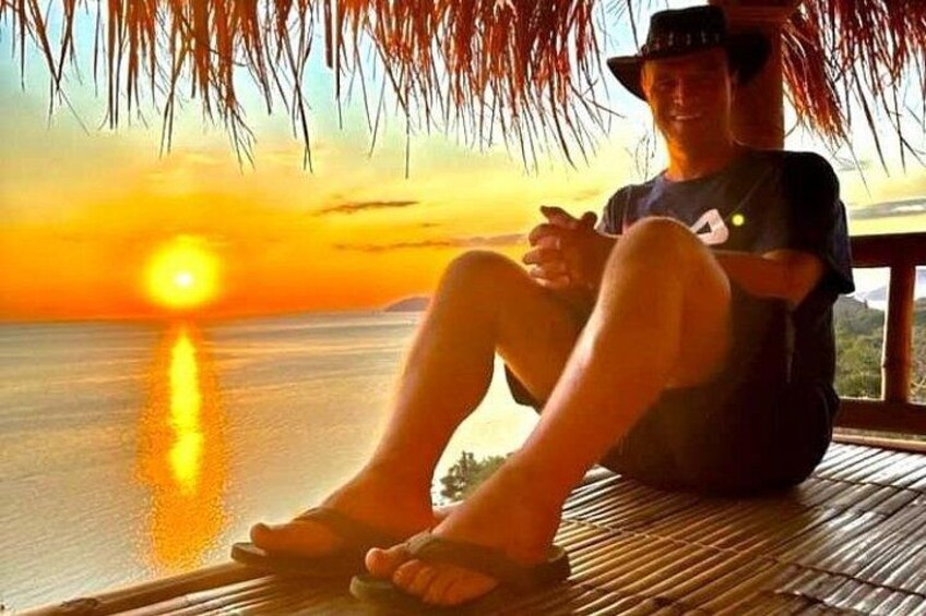 A person sitting on a wooden deck overlooking a body of water during sunset. 4