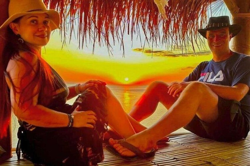 Two people sitting on a wooden deck with a sunset in the background. 3
