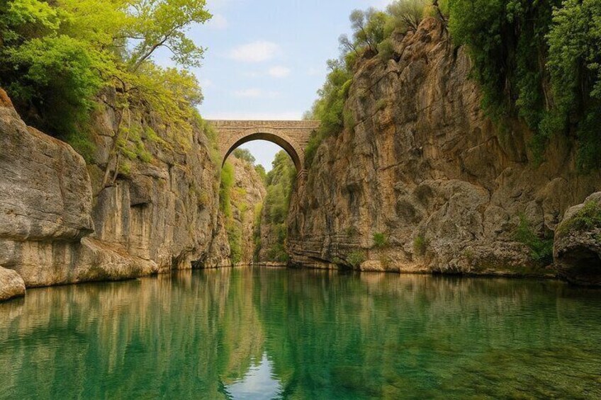Un ponte di pietra che sovrasta un fiume tranquillo, circondato da scogliere rocciose e vegetazione. 2