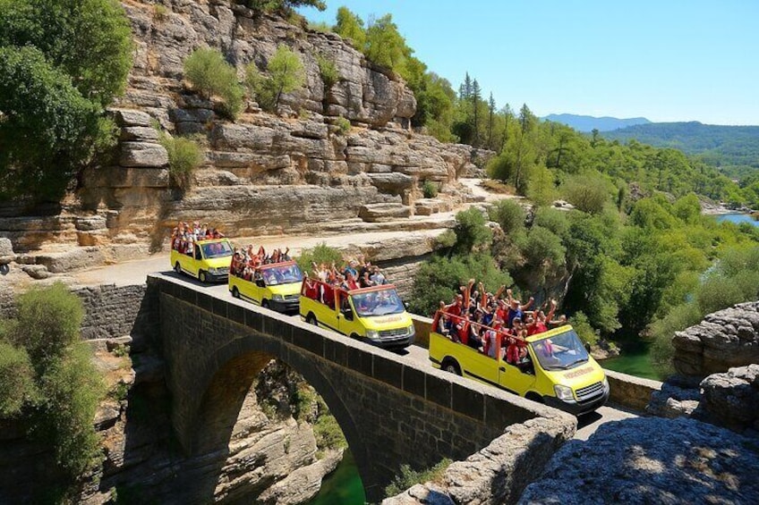 Un autobus giallo turistico su un ponte di pietra, con passeggeri che ammirano il panorama. 3