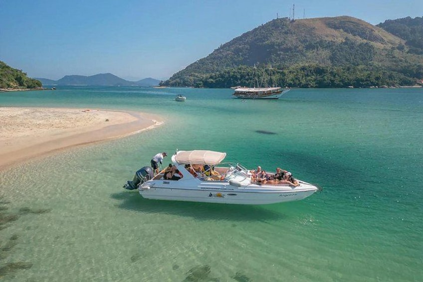 Ein Boot auf einem klaren türkisfarbenen Meer vor einer Sandküste und einer hügeligen Landschaft im Hintergrund. 1