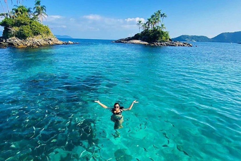 Eine Person schwimmt in klarem türkisblauem Wasser, im Hintergrund sind zwei kleine Inseln zu sehen. 3