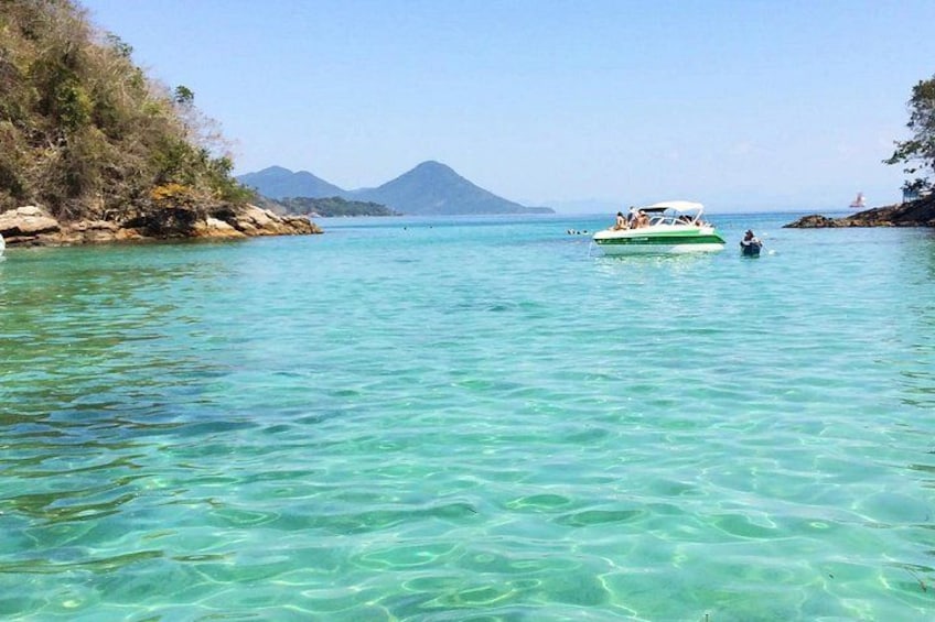 Ein Boot auf klarem türkisblauem Wasser mit einer felsigen Küste und Bergen im Hintergrund. 2