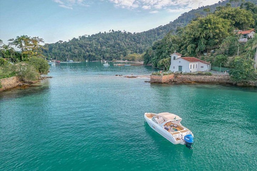 Ein Boot auf einem ruhigen Fluss mit einem Haus am Ufer und einem bewaldeten Hügel im Hintergrund. 2
