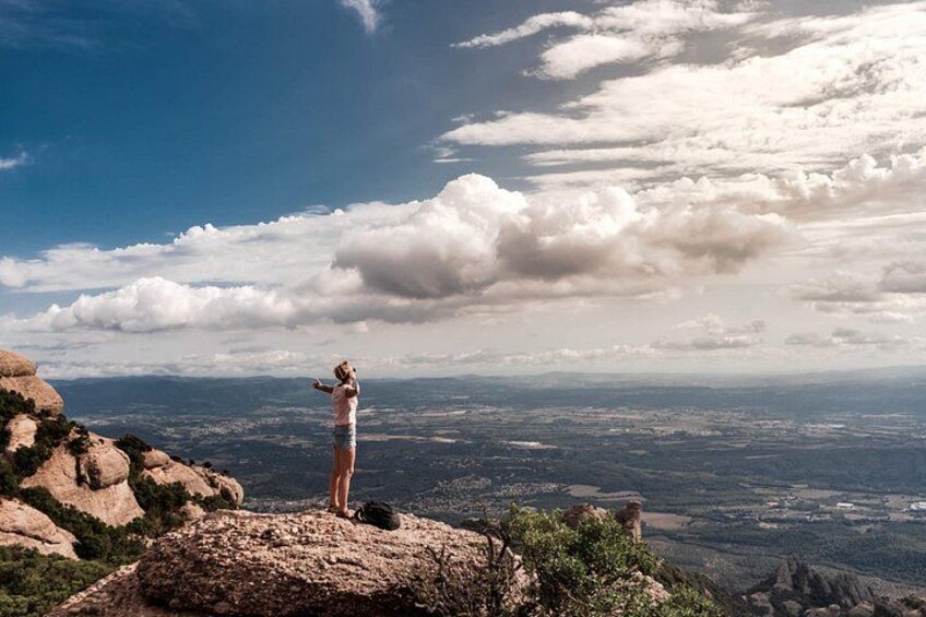 A person standing on a rocky outcrop overlooking a vast landscape with a cloudy sky. 4