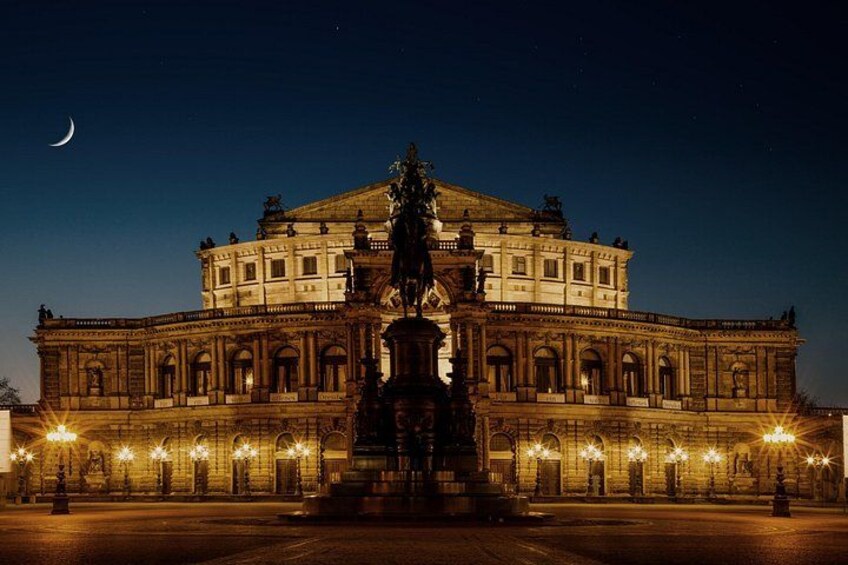 Un imposant bâtiment doté d’une fontaine centrale, illuminé par des lampadaires, se dressant sous un ciel nocturne où brille un croissant de lune. 4