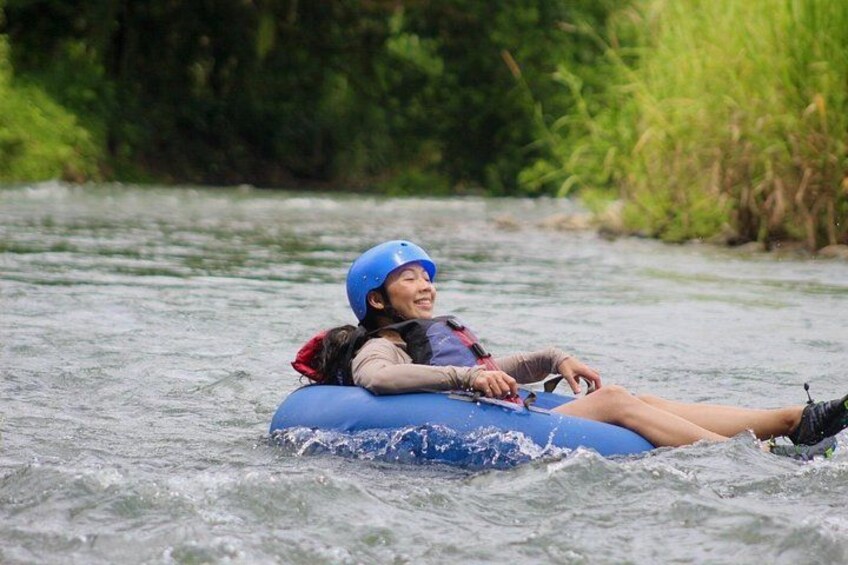 Eine Person in einem blauen Luftmatratzenboot auf einem Fluss, umgeben von viel Grün. 5
