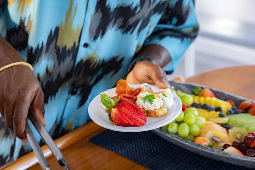 A person holding a plate with a strawberry and a cream-topped item, and a tray with various fruits. 2