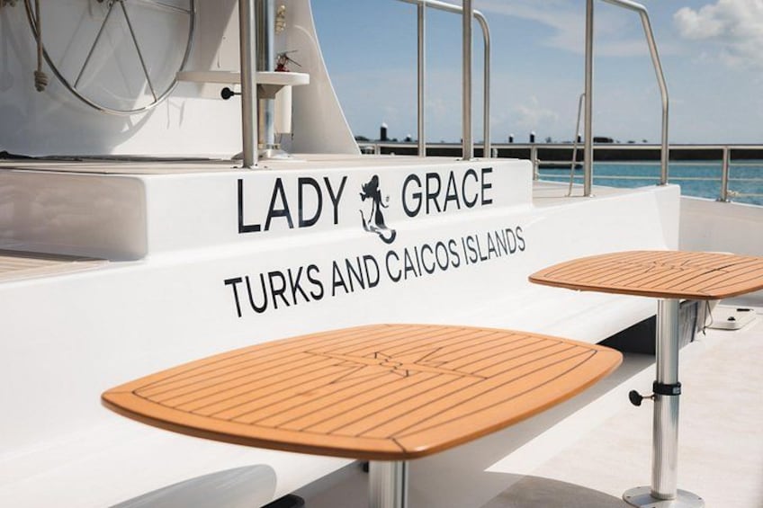 A yacht named 'Lady Grace' with 'Turks and Caicos Islands' written on the side, two wooden tables, and a railing. 4
